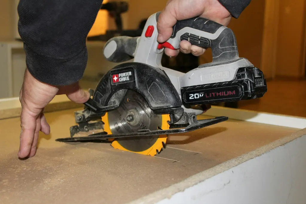 Hands guiding a cordless circular saw through a board in a workshop