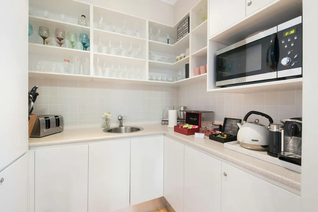 Compact kitchen with white cabinetry, open shelves and a built-in microwave