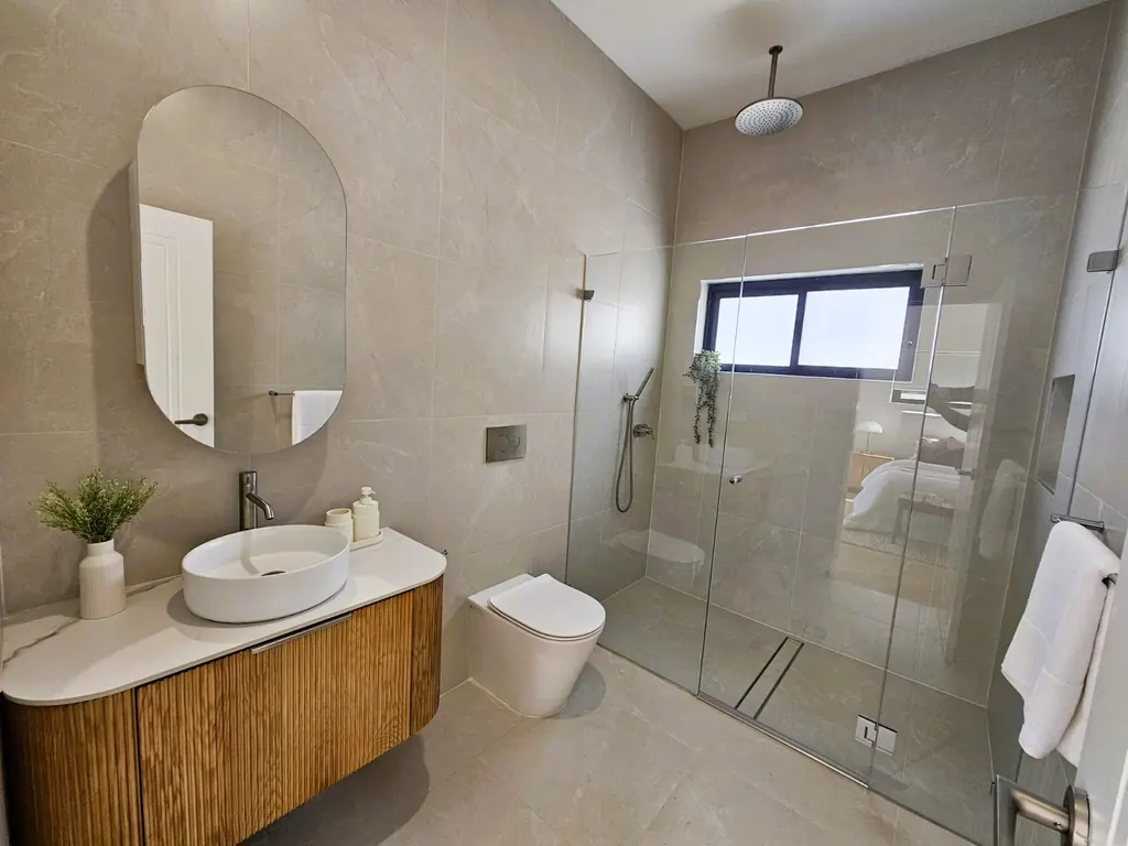 Milestone bathroom with a curved timber vanity, oval mirror and glazed shower