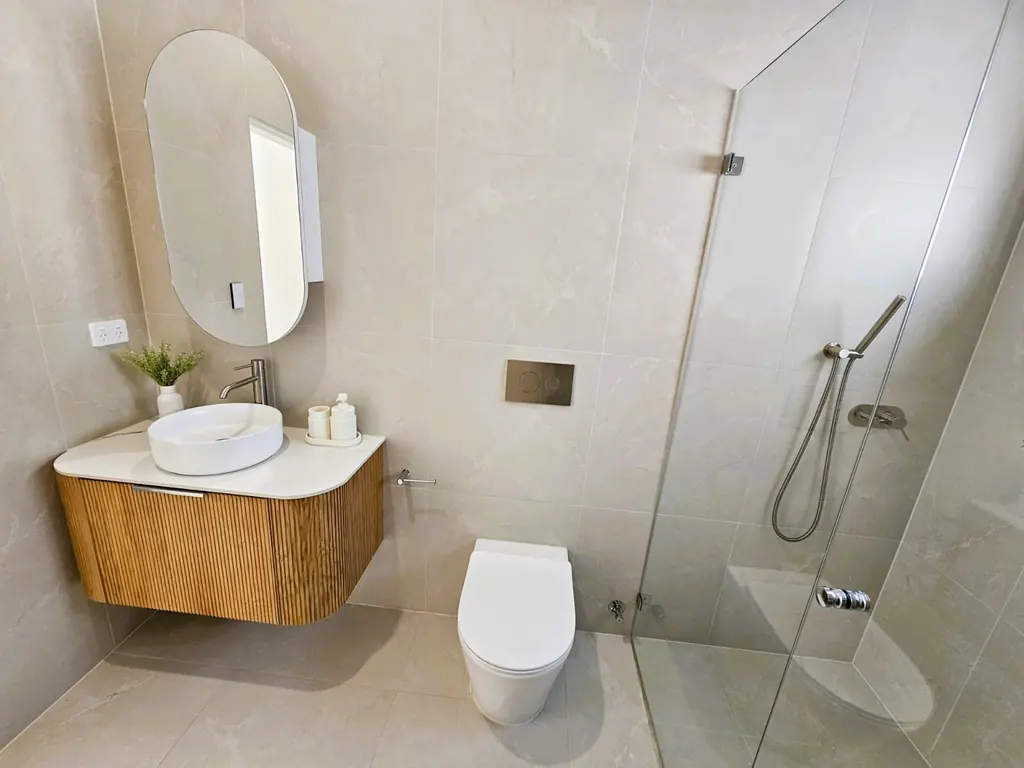 Milestone bathroom with a vessel basin, curved timber vanity and glass shower screen