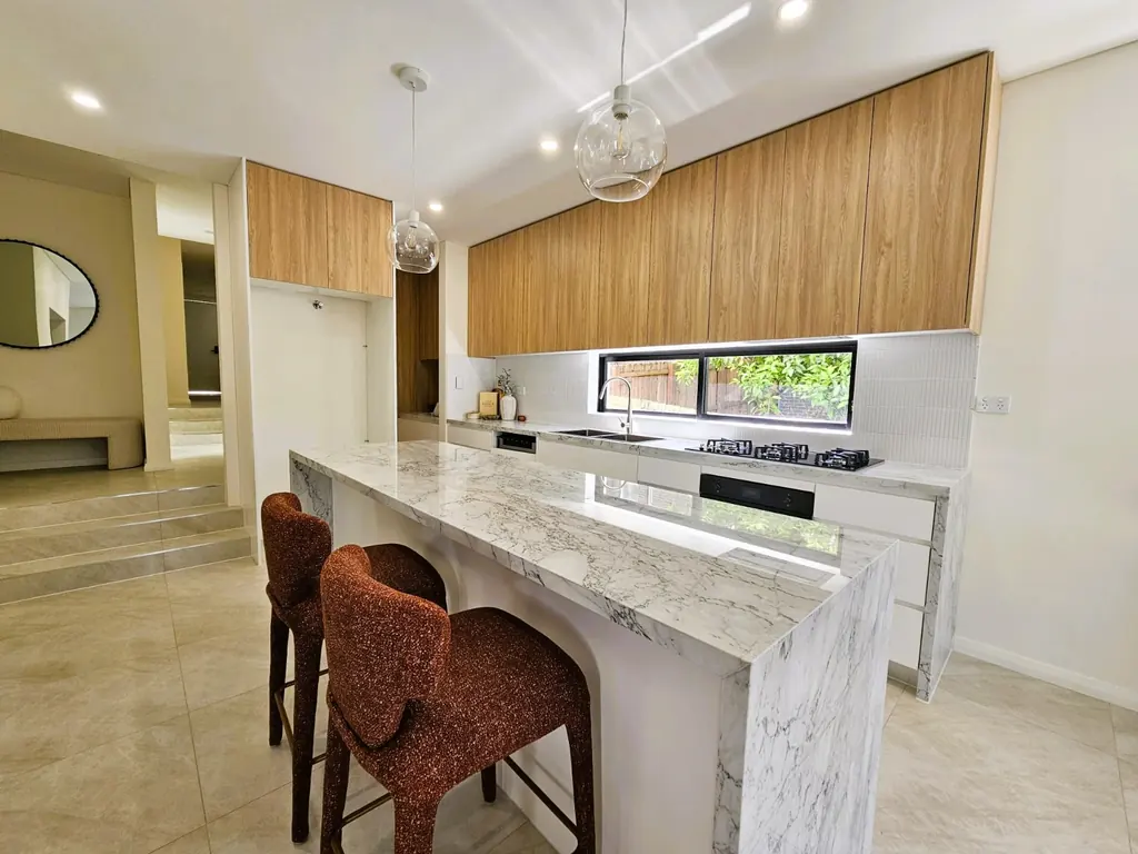 Milestone kitchen with timber cabinetry, a veined island and pendant lights