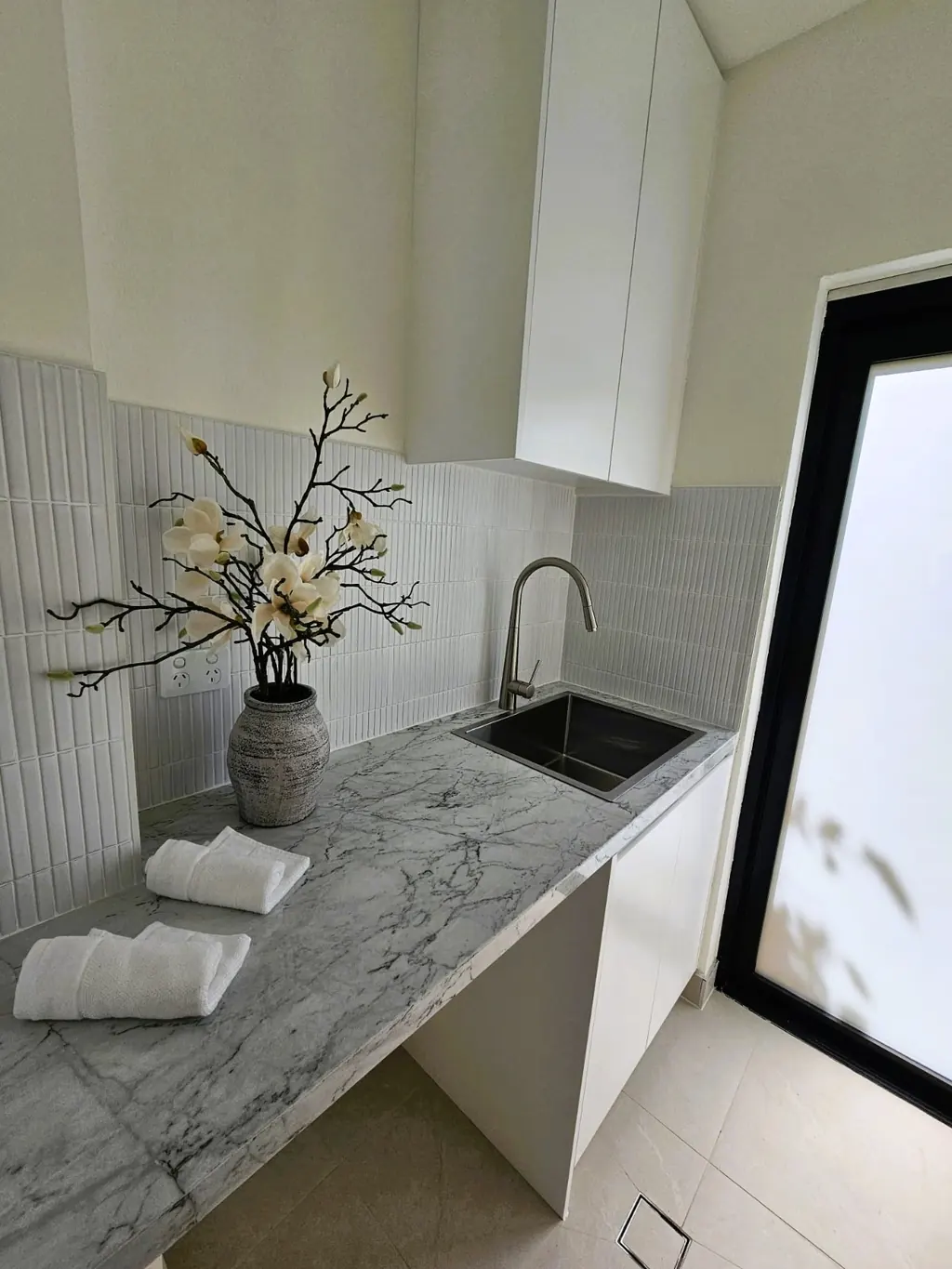 Milestone utility space with a sink, tiled splashback and pale cabinetry